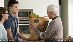 young people handing older man bag of groceries