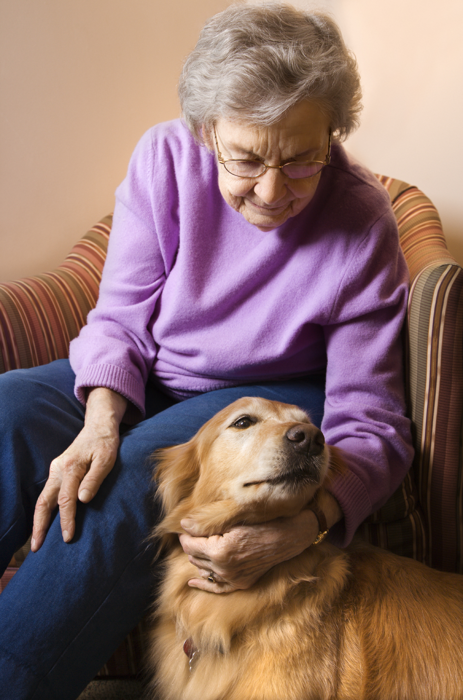 An Older Woman Sitting in a Chair Petting Her Dog