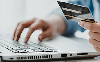 Person typing on laptop holding a credit card